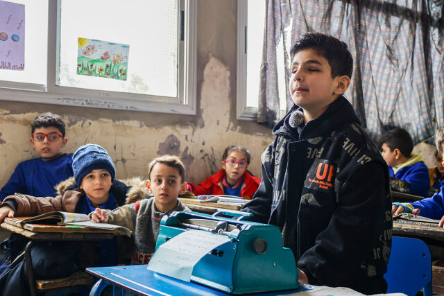 Sokea lapsi seisoo keskellä luokkaa edessään braille-laite.