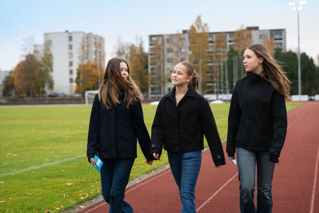 Kolme nuorta kävelee urheilukentällä.