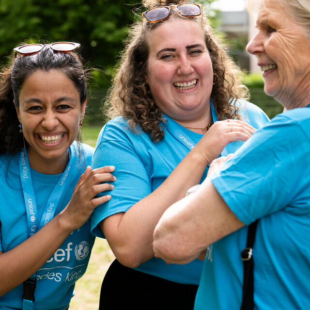 Three people with UNICEF shirts laugh.