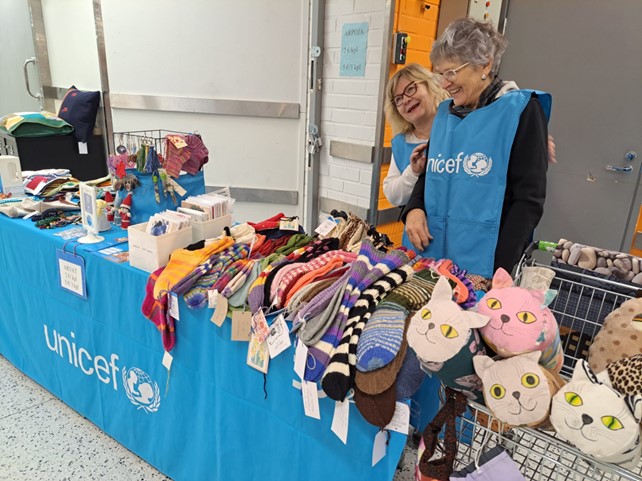 Kaksi UNICEFin vapaaehtoista myyntipöydän äärellä.