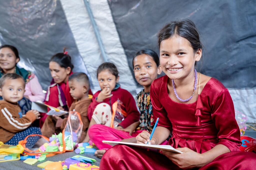 Nepalilaisia lapsia istumassa UNICEFin teltassa piirtämässä värikynillä.