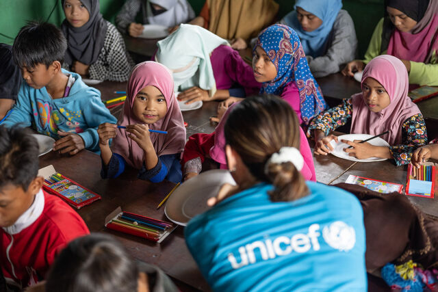 UNICEFin työntekijä juttelee lasten kanssa koulussa.