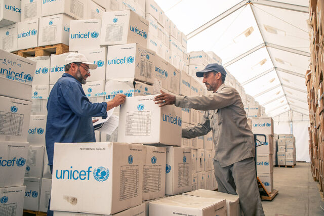 Kaksi lastaa ottaa vettä vesihanasta ulkona. Taustalla säiliö, jossa UNICEFin logo.