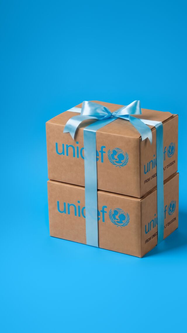 Lahjannauhalla koristeltu paketti UNICEFin hätäaputarvikkeita sinistä taustaa vasten.